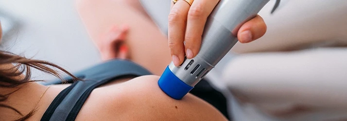 A close-up of a handheld device applying laser therapy to a person’s shoulder.